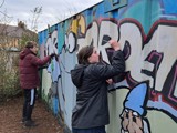 Two people from the group painting large storage container at the allotment 
