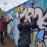 Two people from the group painting large storage container at the allotment 